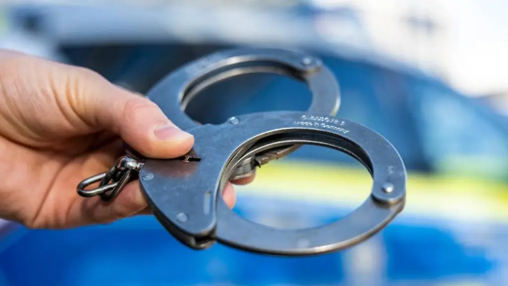 Eine-Hand-haelt-Handschellen-vor-einem-Polizeifahrzeug