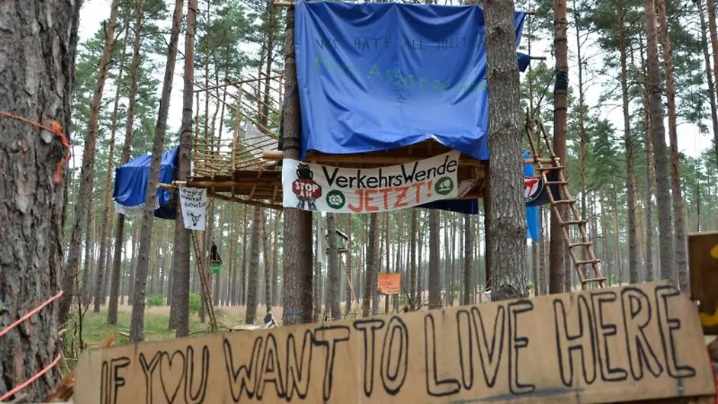 Blick-auf-Baumhaeuser-und-Plakate-eines-mit-dem-Schriftzug-Verkehrswende-jetzt
