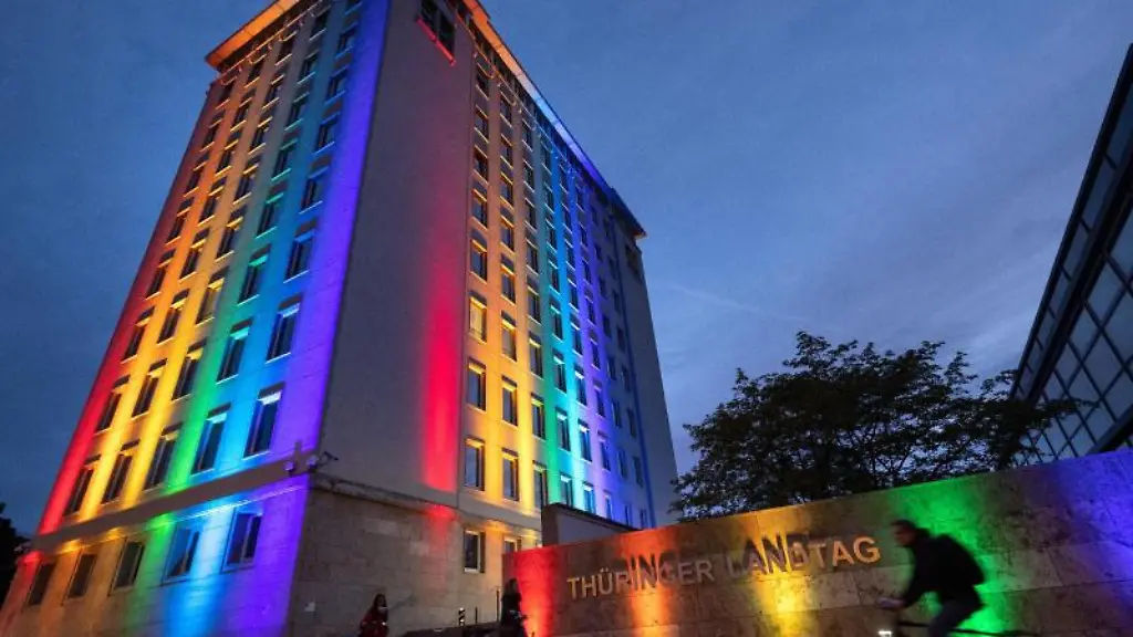 Radfahrer-passieren-den-in-Regenbogenfarben-angestrahlten-Landtag