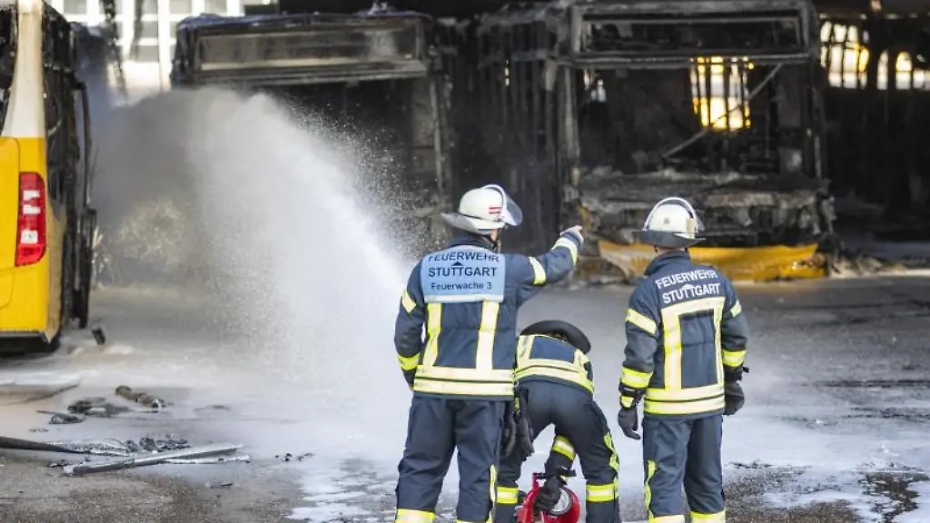 Feuerwehrmaenner-stehen-bei-Nachloescharbeiten-vor-ausgebrannte-Bussen
