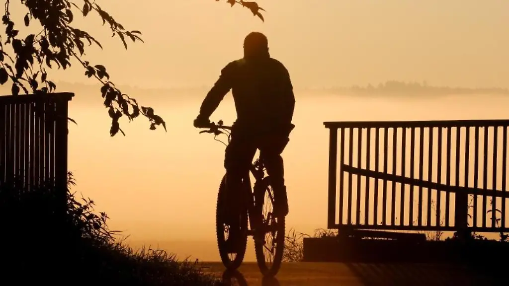 Ein-Radfahrer-faehrt-bei-Sonnenaufgang-ueber-eine-Bruecke