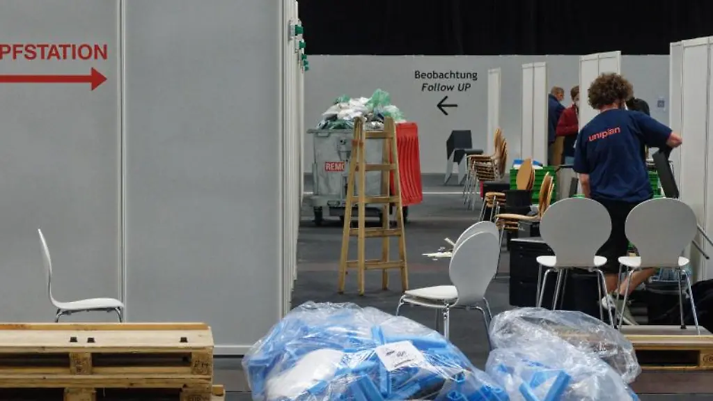 Arbeiter-tragen-im-Impfzentrum-in-Koeln-Einrichtungsgegenstaende-aus-den-Impfkabinen