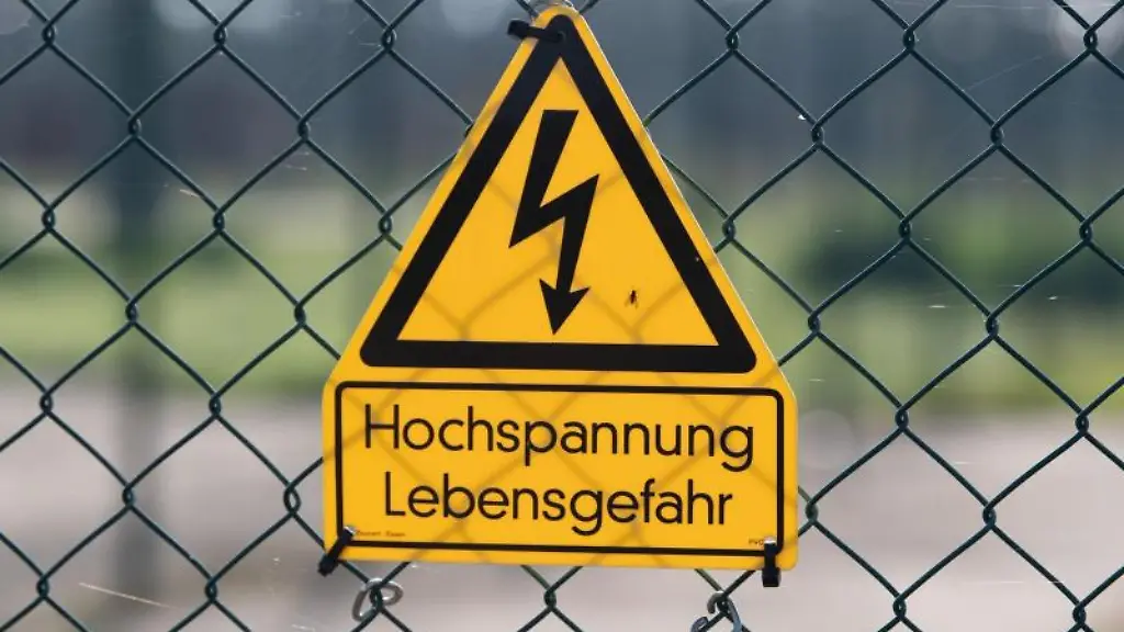 Ein-Schild-mit-der-Aufschrift-Hochspannung-Lebensgefahr-haengt-an-einem-Zaun-vor-dem-Gelaende-eines-Umspannwerks