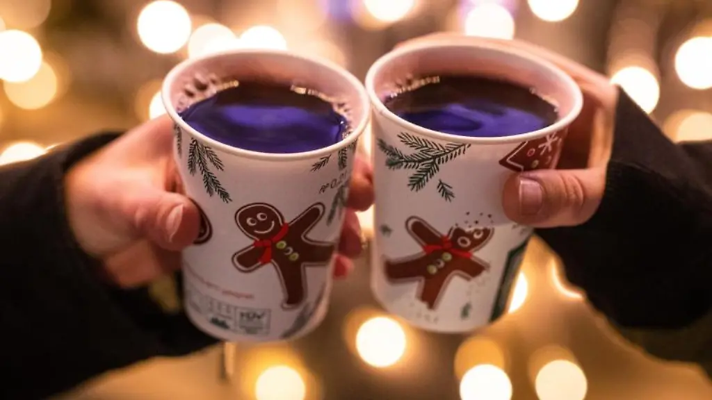 Zwei-Frauen-stossen-mit-Gluehwein-gefuellten-Bechern-auf-einem-Weihnachtsmarkt-an