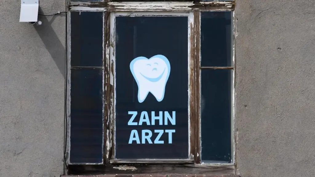 Zahnarzt-steht-an-einem-Fenster-eines-Hauses-in-dem-sich-eine-Zahnarztpraxis-befindet