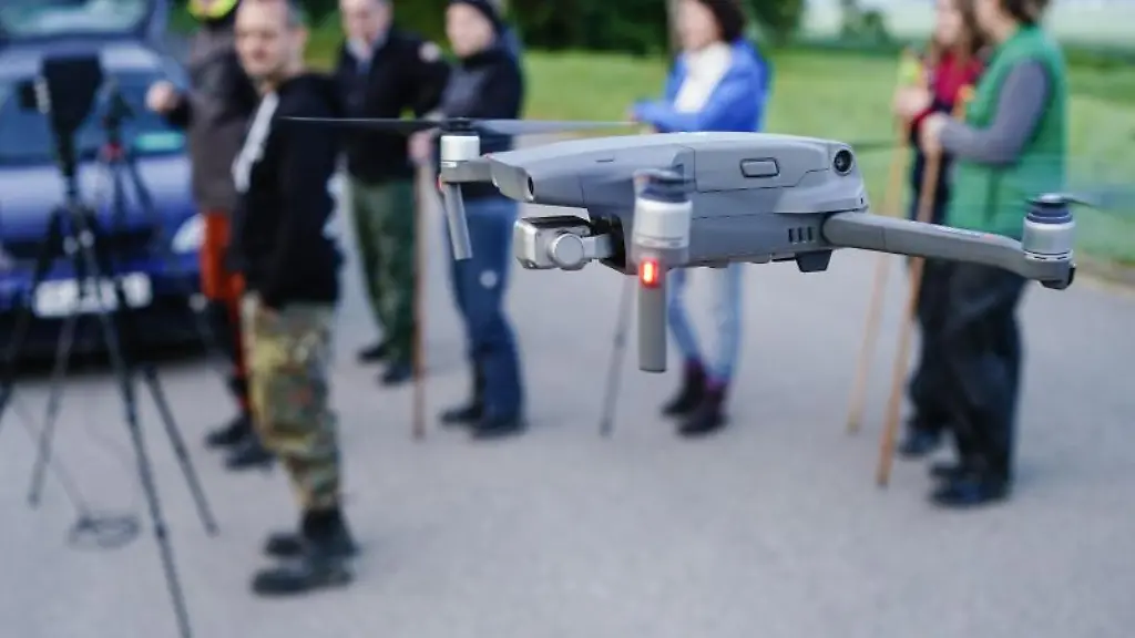 Helfer-der-Rehkitz-Rettung-stehen-hinter-einer-sich-im-Flug-befindlichen-Drohne-mit-Waermebildkamera