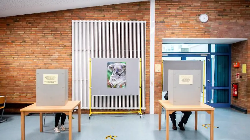 Eine-Waehlerin-und-ein-Waehler-sitzen-in-einem-Wahllokal-in-der-Wahlkabine