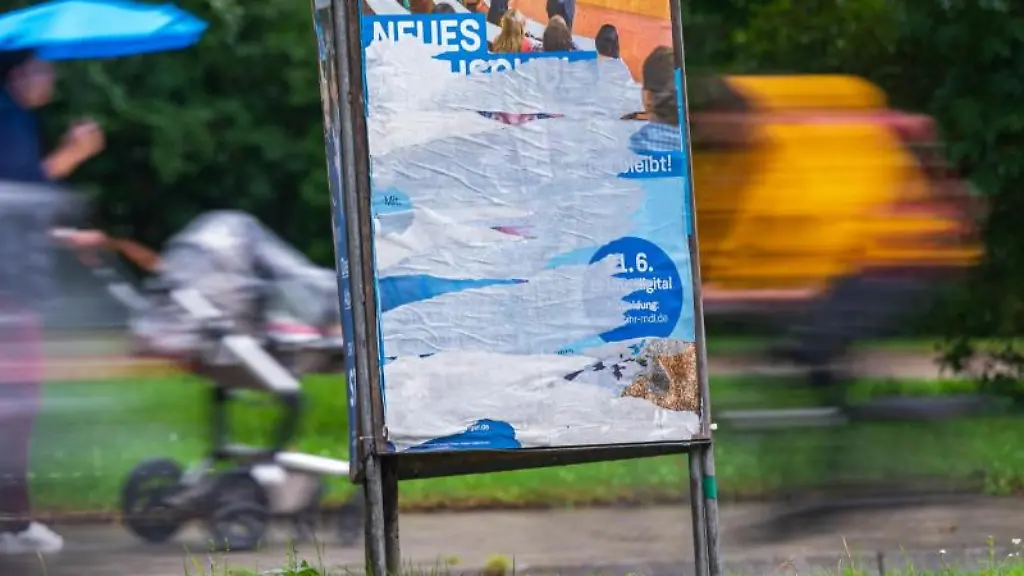 Personen-gehen-an-einem-beschaedigtem-Wahlplakat-vorbei-das-am-Strassenrand-steht