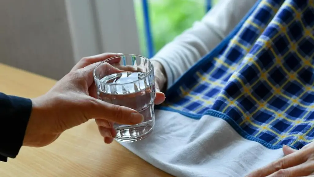 Eine-Pflegerin-reicht-einer-alten-Frau-ein-Glas-Wasser