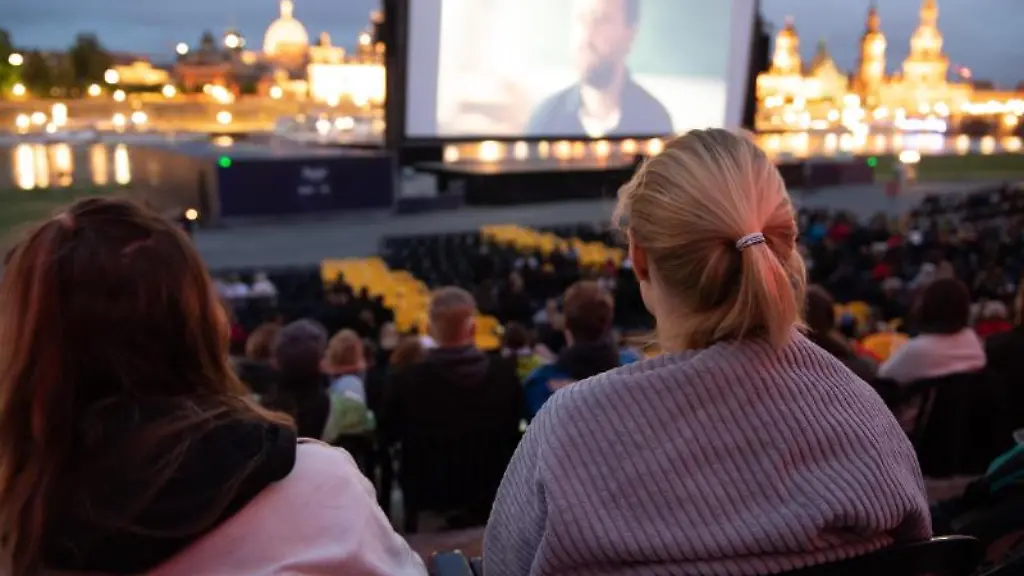 Zahlreiche-Gaeste-der-Filmnaechte-am-Elbufer-sitzen-vor-der-Kulisse-der-Dresdner-Altstadt-und-schauen-auf-eine-Kinoleinwand