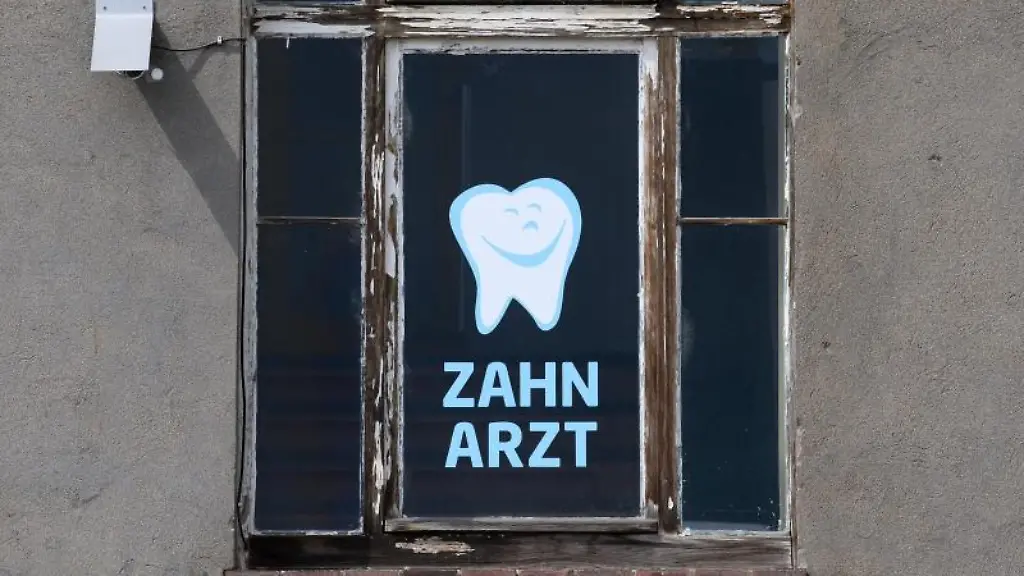 Zahnarzt-steht-an-einem-Fenster-eines-Hauses-in-dem-sich-eine-Zahnarztpraxis-befindet