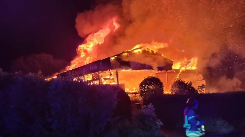 Ein-Feuerwehrmann-laeuft-vor-einem-in-Flammen-stehenden-Supermarkt