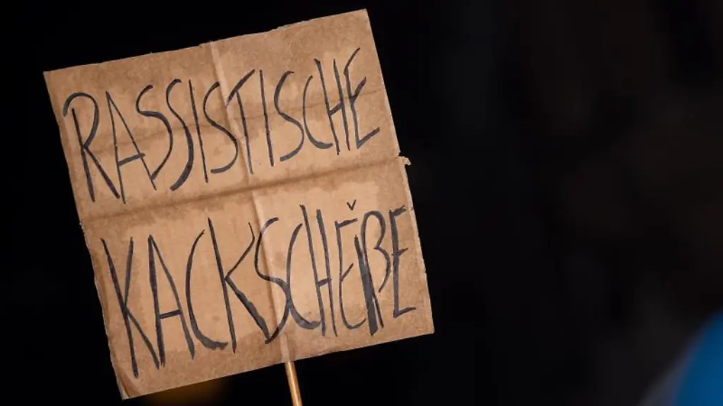 Ein-Schild-mit-der-Aufschrift-Rassistische-Kackscheisse-wird-auf-einer-Demonstration-in-die-Hoehe-gehalten