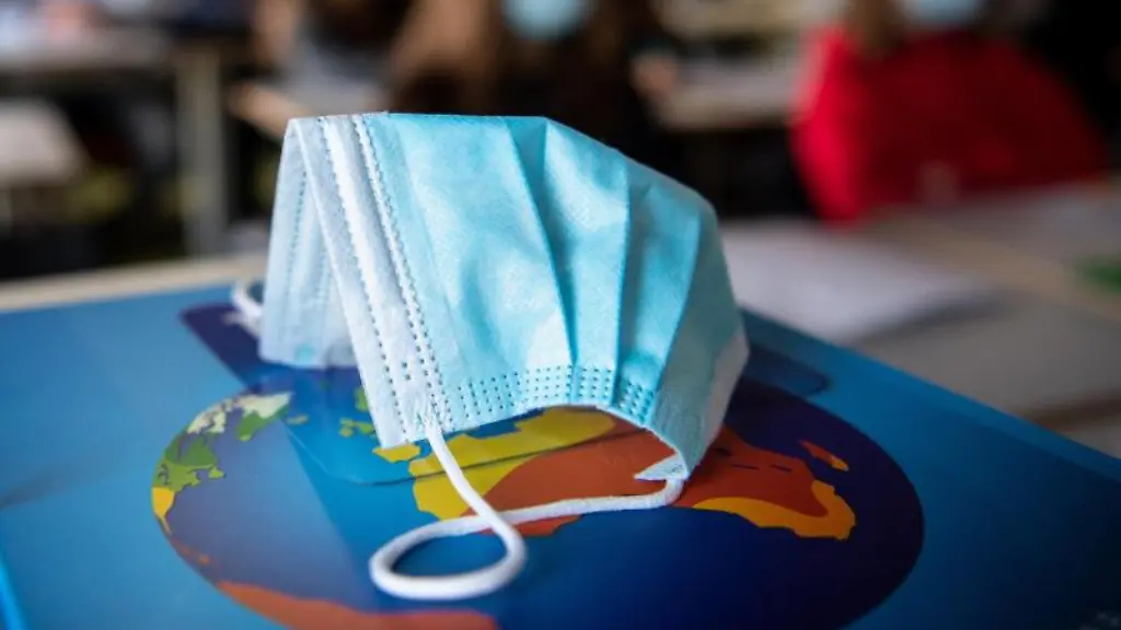 Ein-Mund-Nasen-Schutz-liegt-waehrend-des-Unterrichts-auf-einem-Atlas