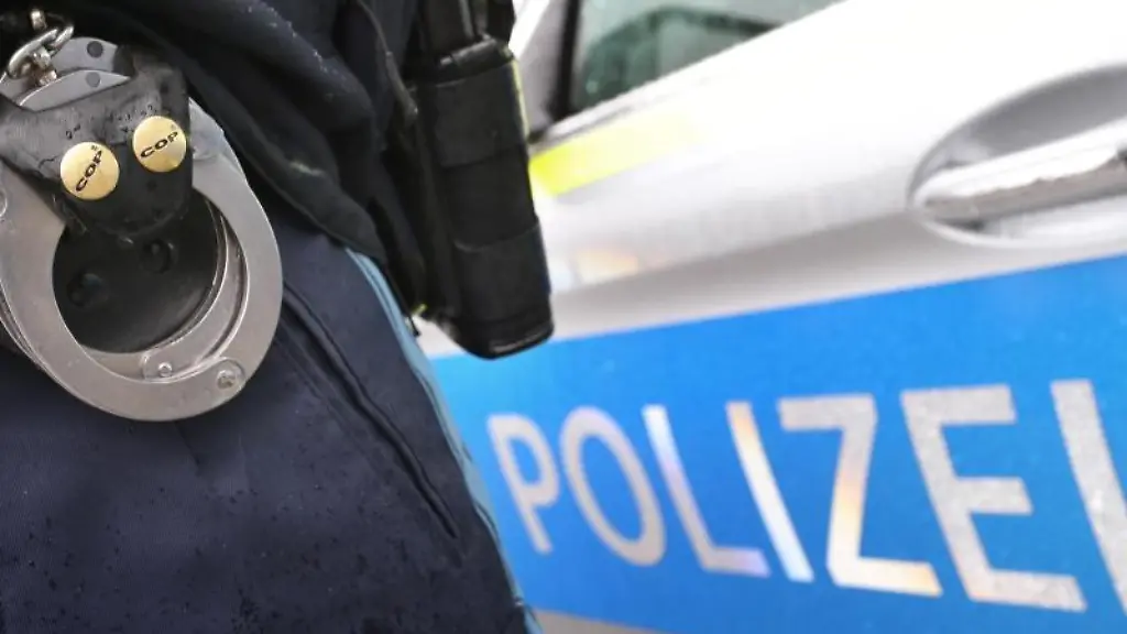 Ein-Polizist-mit-Handschellen-und-einer-Pistole-am-Guertel-steht-vor-einem-Streifenwagen
