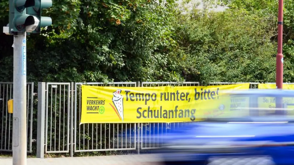 Ein-Auto-faehrt-an-einem-Transparent-Tempo-runter-bitte-Schulanfang-vorbei