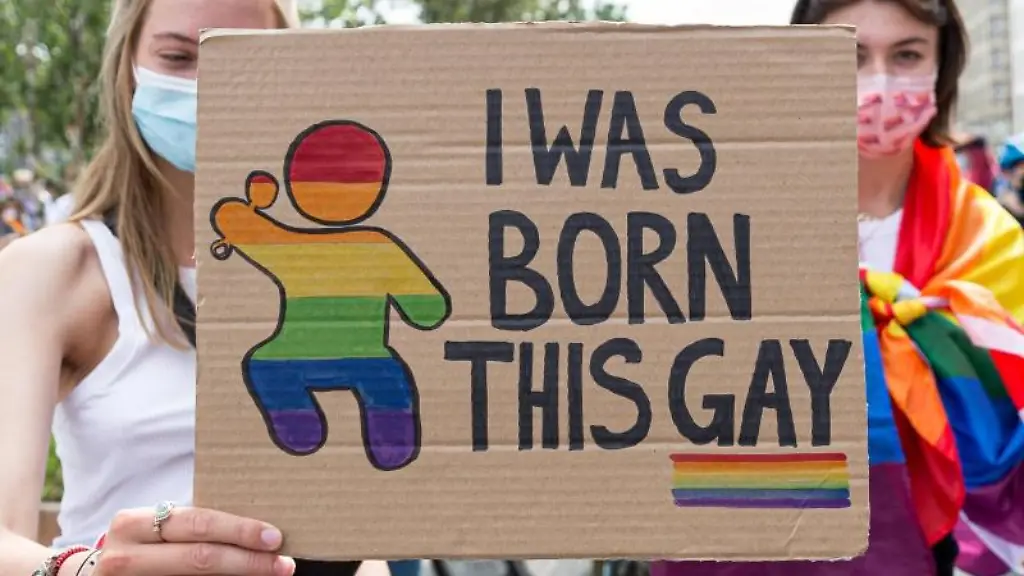 Eine-junge-Frau-haelt-auf-einer-CSD-Fahrraddemo-ein-Schild-mit-der-Aufschrift-I-was-born-this-gay