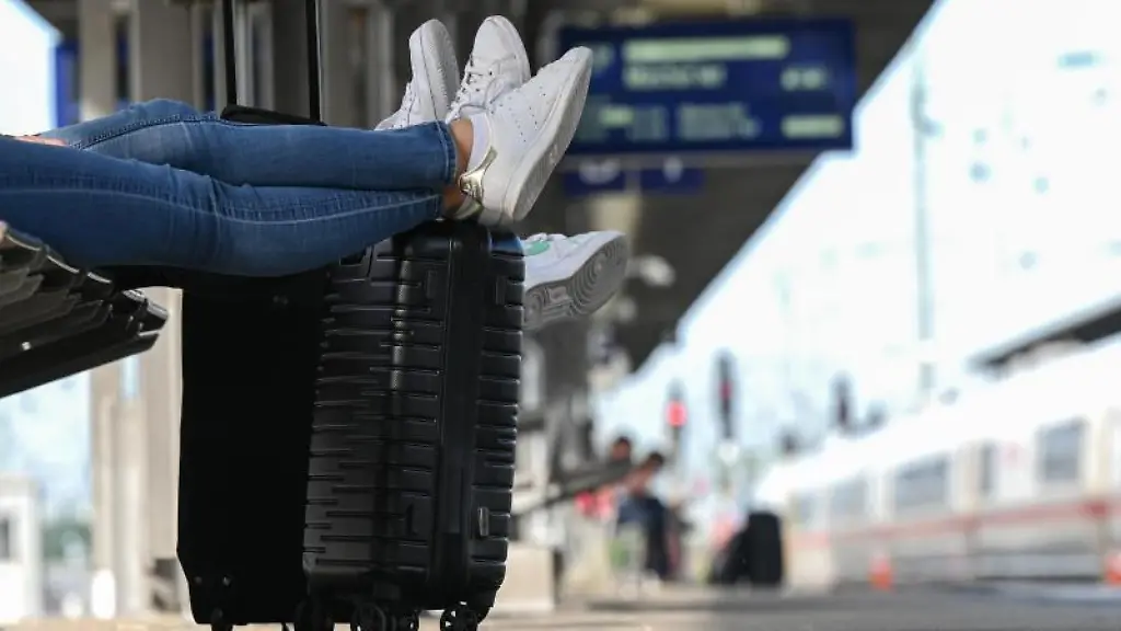 Zwei-Reisegaeste-warten-an-einem-Bahnhof-am-Gleis