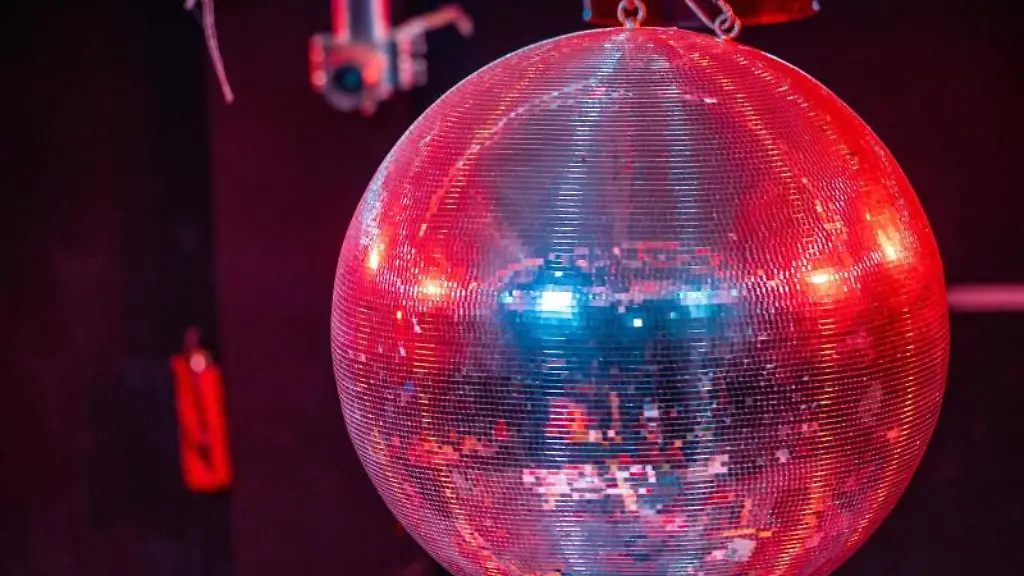 Eine-farbig-beleuchtete-Discokugel-dreht-sich-ueber-der-Tanzflaeche-in-einer-Diskothek