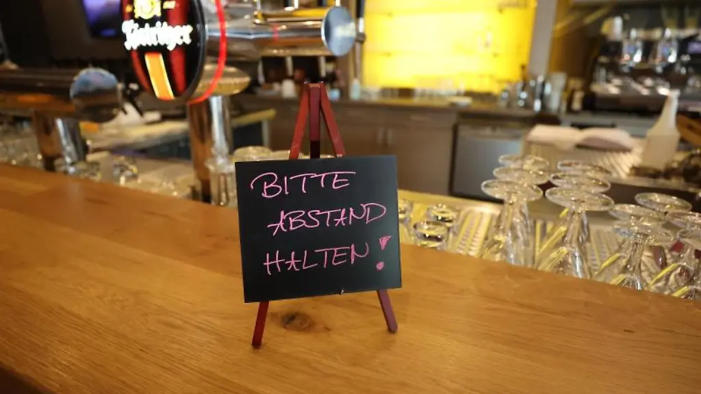 Ein-Schild-mit-der-Aufschrift-Bitte-Abstand-halten-steht-auf-dem-Tresen-in-einem-Bierhaus