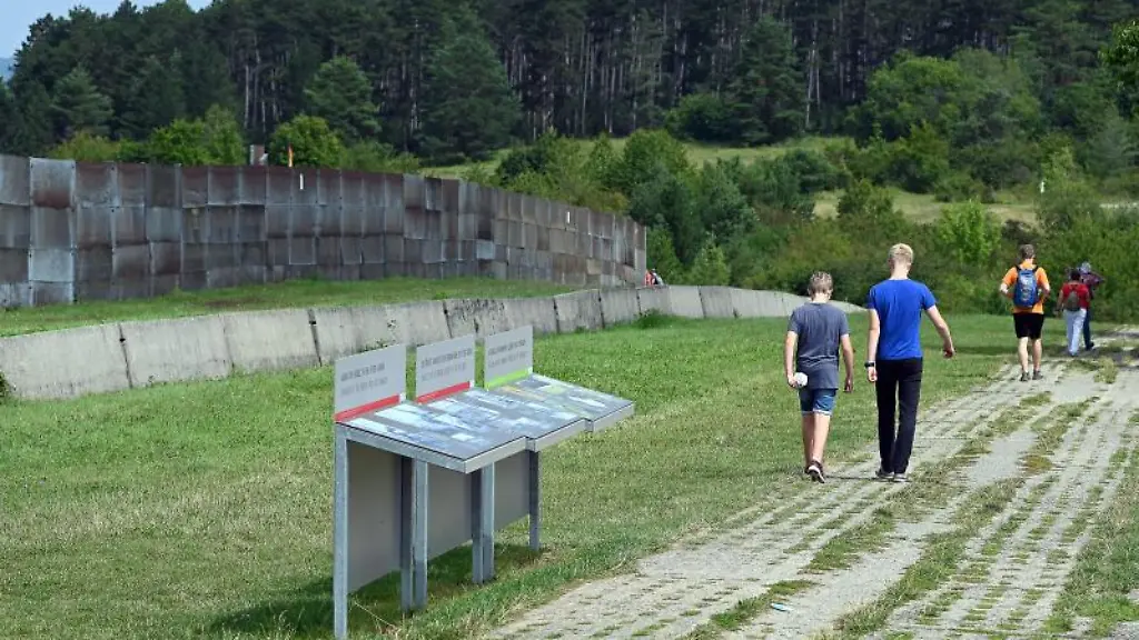 Besucher-gehen-auf-dem-ehemaligen-Kolonnenweg-neben-einem-Grenzzaun-an-der-Gedenkstaette-Point-Alpha-entlang