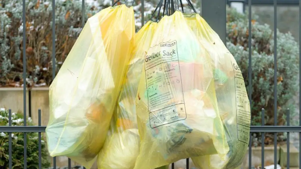 Vier-gelbe-Muellsaecke-haengen-aussen-an-einem-Gartenzaun-zur-Abholung-bereit