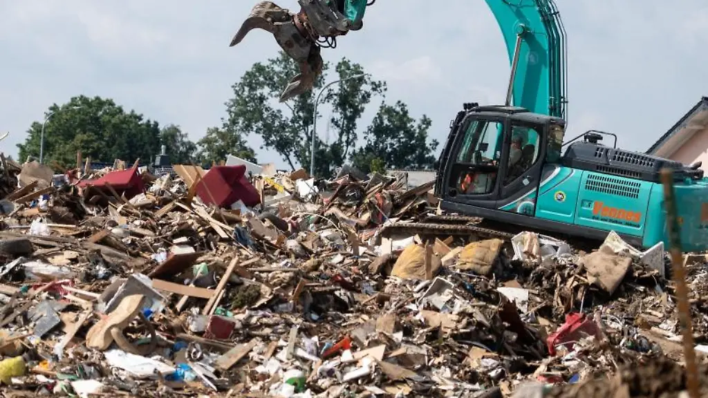Ein-Bagger-faehrt-auf-einem-riesigen-Muellberg-auf-einer-Wiese-vor-dem-Ort