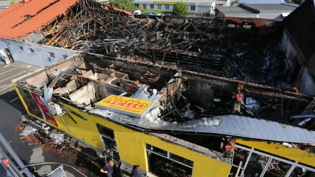 Einsatzkraefte-der-Feuerwehr-stehen-neben-einem-ausgebrannten-Supermarkt