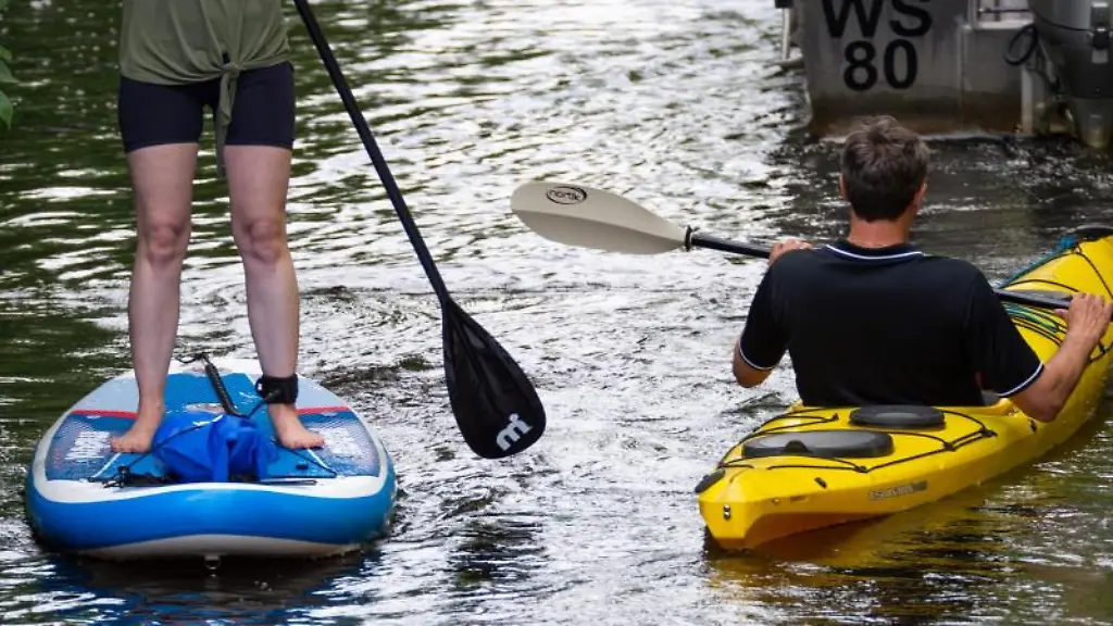 Eine-Stand-Up-Paddlerin-und-ein-Kajak-Fahrer-gleiten-auf-einem-Alsterkanal-dicht-aneinander-vorbei