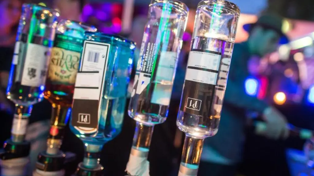 Hochprozentige-alkoholische-Getraenke-sind-an-einer-Bar-zu-sehen-waehrend-im-Hintergrund-ein-Barkeeper-ein-Getraenk-mixt