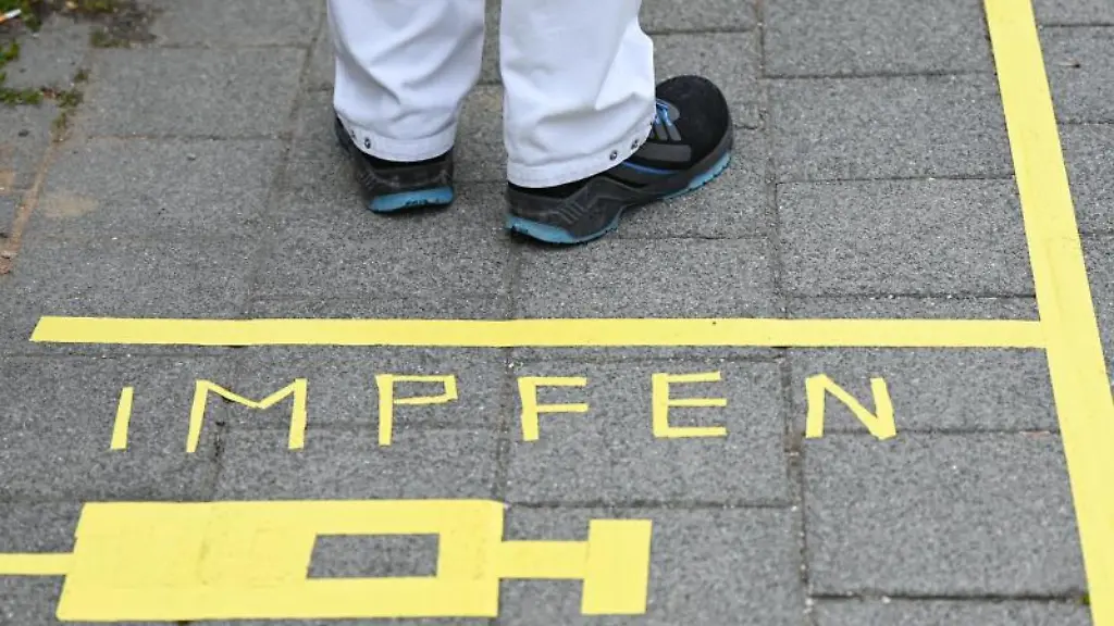 Ein-Mann-steht-am-Covid-19-Impfcenter-hinter-einer-Bodenmarkierung-mit-der-Aufschrift-Impfen-und-einer-Spritze