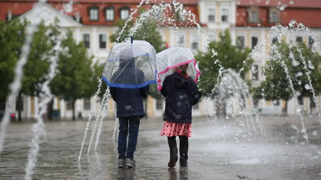 Zwei-Kinder-geht-mit-Schirmen-bei-Regenwetter-durch-ein-Wasserspiel-auf-dem-Domplatz