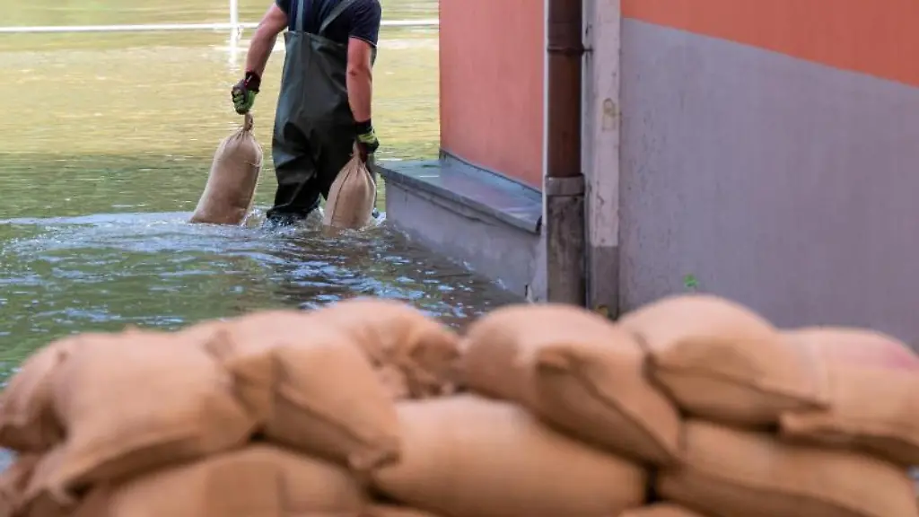 Ein-Mann-traegt-Sandsaecke-um-Abdichten-von-Tueren-und-Fenstern-durch-das-Wasser-der-Donau-das-auf-der-Uferpromenade-steht