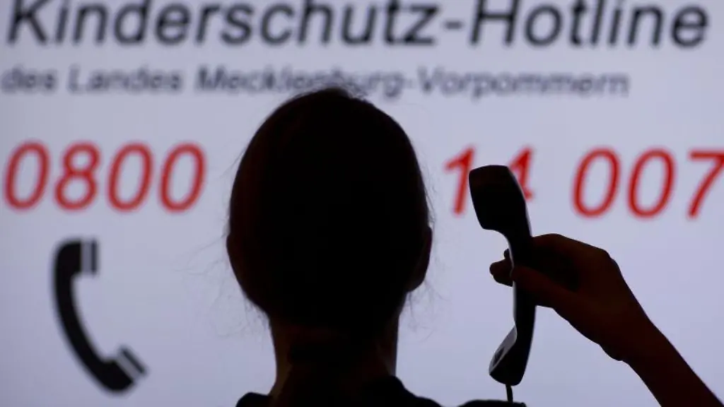 Ein-Maedchen-haelt-in-Schwerin-einen-Telefonhoerer-vor-einer-Informationstafel-der-Kinderschutz-Hotline