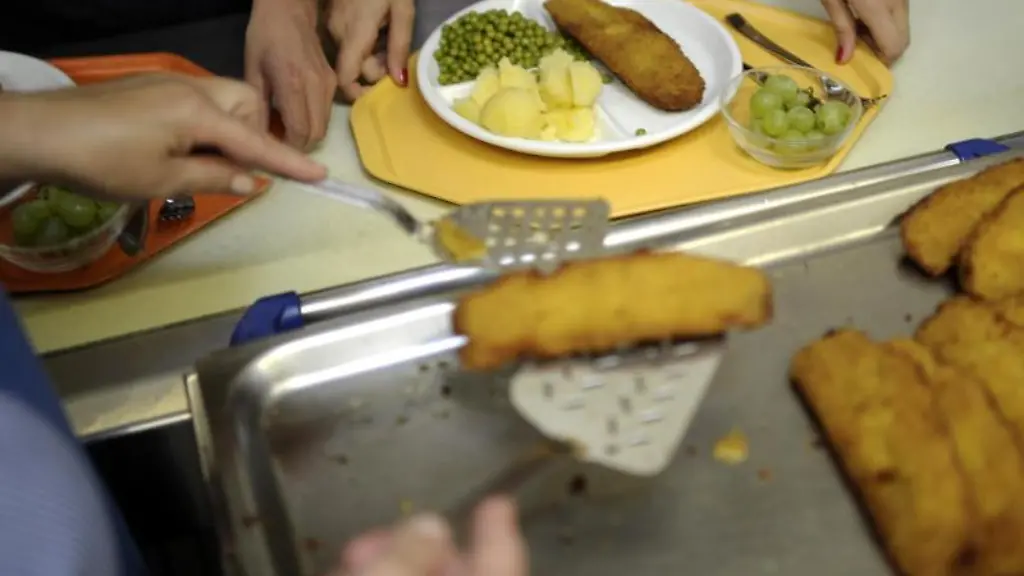 Eine-Kuechenhelferin-legt-an-einer-Gesamtschule-ein-Stueck-Fisch-auf-einen-Teller-eines-Schuelers