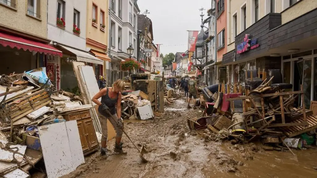 Anwohner-und-Ladeninhaber-versuchen-ihre-Haeuser-vom-Schlamm-zu-befreien-und-unbrauchbares-Mobiliar-nach-draussen-zu-bringen