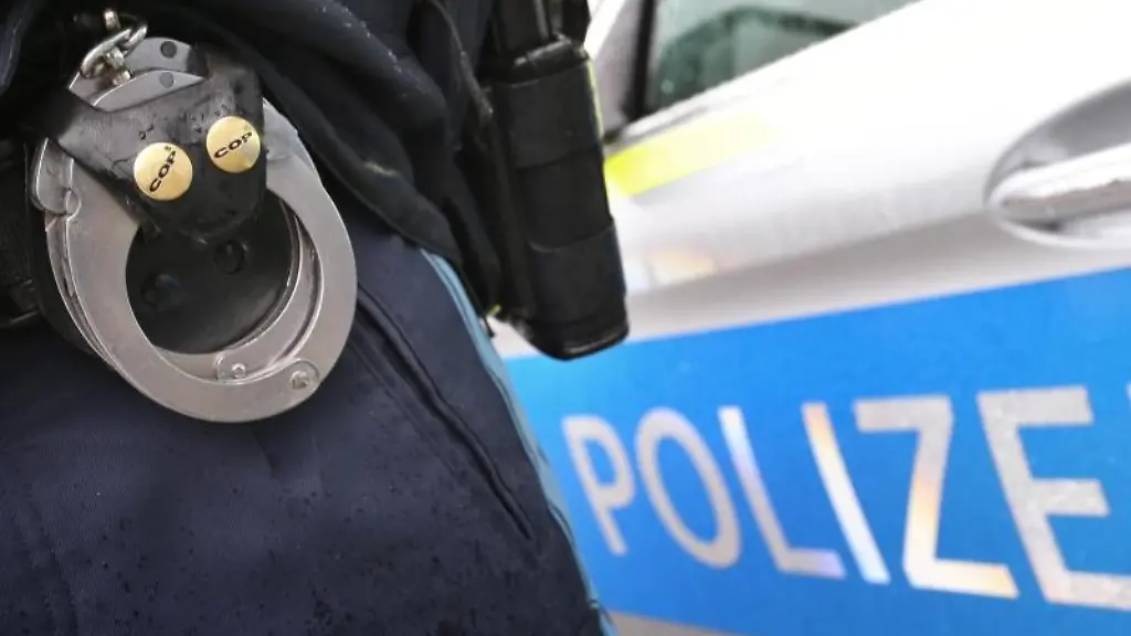 Ein-Polizist-mit-Handschellen-und-einer-Pistole-am-Guertel-steht-vor-einem-Streifenwagen