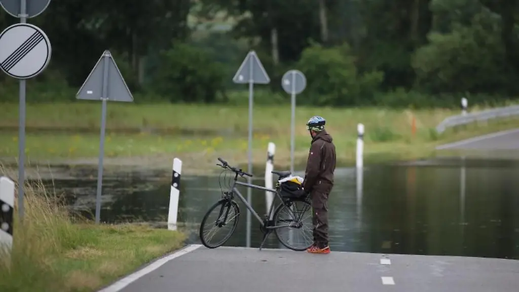 Ein-Radfahrer-steht-an-einer-ueberfluteten-Strasse