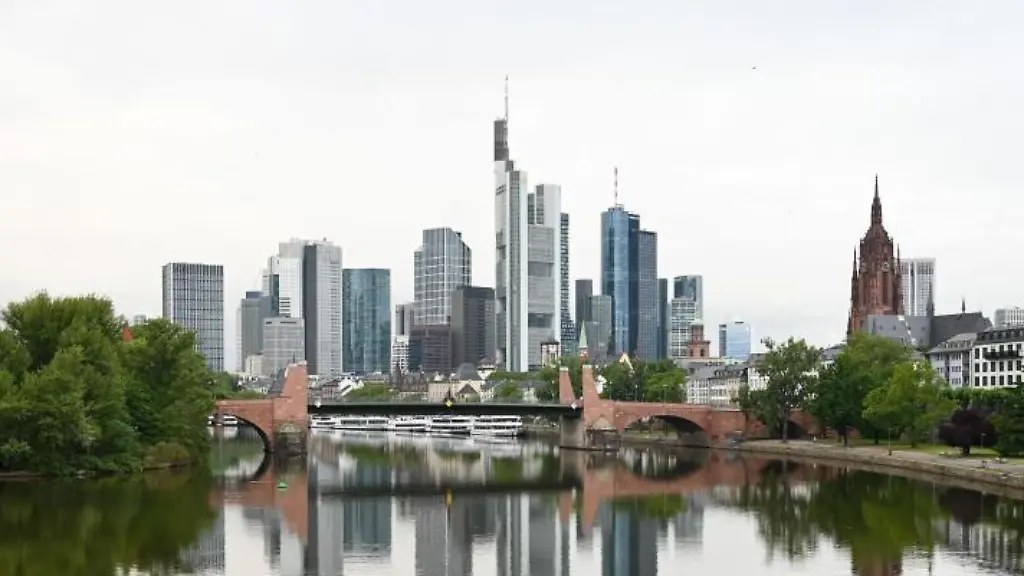 Die-Frankfurter-Skyline-mit-ihren-markanten-Bankentuermen-spiegelt-sich-am-Morgen-im-Wasser-des-Mains