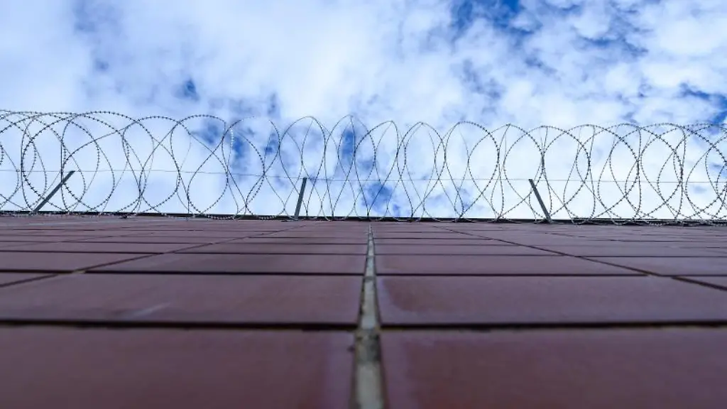 Ein-Stacheldrahtzaun-haengt-an-einer-Mauer-einer-Justizvollzugsanstalt