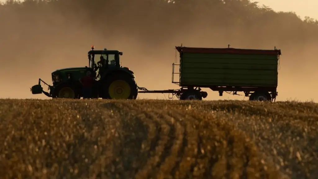 Ein-Traktor-steht-bei-Sonnenuntergang-mit-einem-Anhaenger-auf-einem-abgeernteten-Feld