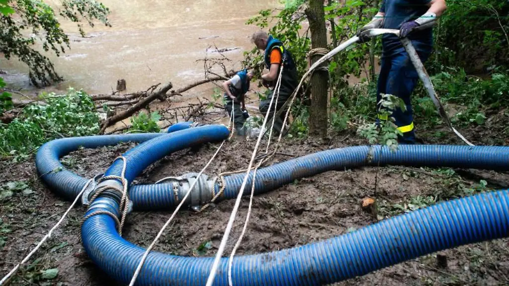 Mitarbeiter-des-THW-legen-an-einem-Damm-an-einem-Rueckhaltebecken-das-zu-brechen-droht-Schlaeuche-und-pumpen-das-Wasser-ab
