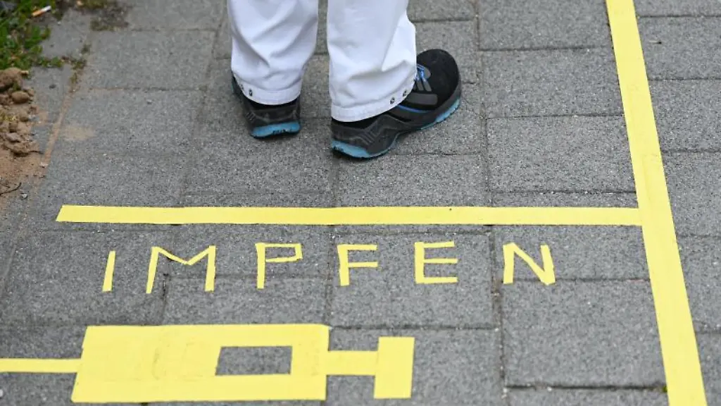 Ein-Mann-steht-am-Covid-19-Impfcenter-hinter-einer-Bodenmarkierung-mit-der-Aufschrift-Impfen-und-einer-Spritze