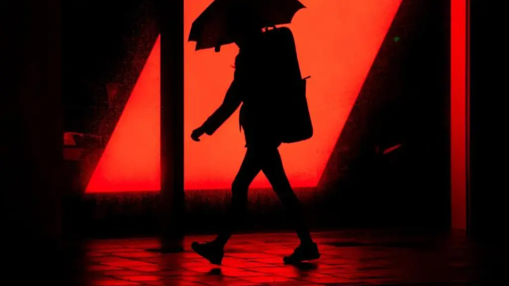 Eine-Frau-laeuft-mit-ihrem-Schirm-im-Regen-an-der-Leuchtreklame-eines-Autohauses-entlang