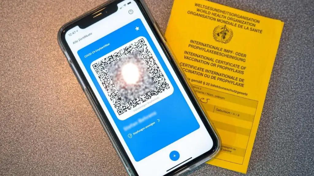 Ein-Smartphone-mit-dem-QR-Code-eines-digitalen-Impfausweises-liegt-zusammen-mit-einem-Impfbuch-auf-dem-Tisch