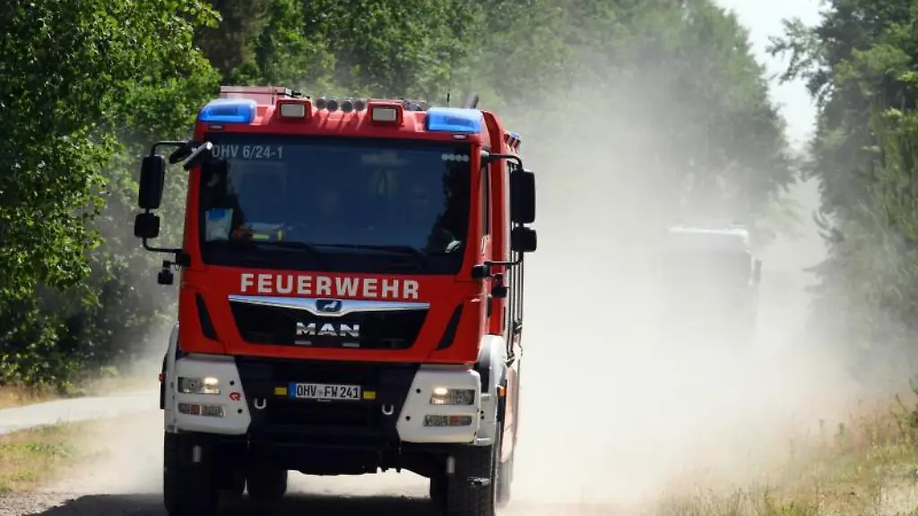 Ein-Fahrzeug-der-Feuerwehr-Oberhavel-faehrt-auf-dem-sandigen-Weg-durch-den-Wald-und-zieht-eine-Staubfahne-hinter-sich-her