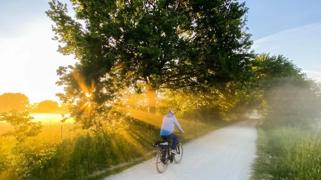 Ein-Mann-faehrt-mit-einem-Fahrrad-um-5-40-Uhr-bei-Sonnenaufgang-und-leichten-Bodennebel-durch-die-Leinemasch-in-der-Region-Hannover