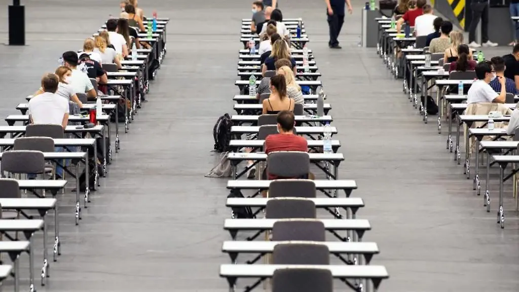 Studenten-und-Studentinnen-sitzen-an-Tischen-in-einer-Messehalle-und-warten-auf-ihre-Klausur