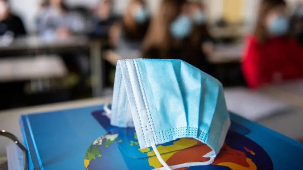 Ein-Mund-Nasen-Schutz-liegt-waehrend-des-Unterrichts-auf-einem-Atlas