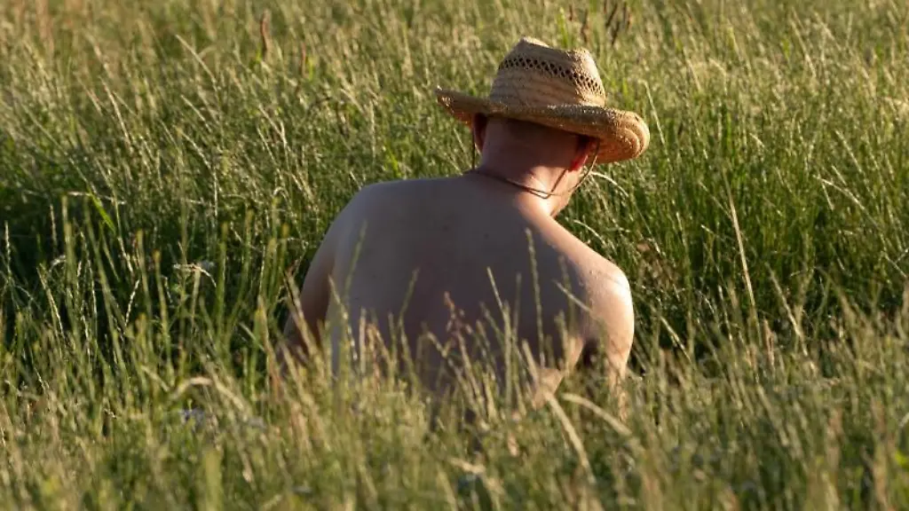 Ein-Mann-mit-Strohhut-sitzt-auf-einer-Wiese
